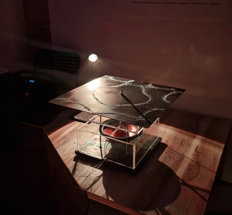 The Chladni plate, spotlit, with sand tracing its resonant pattern